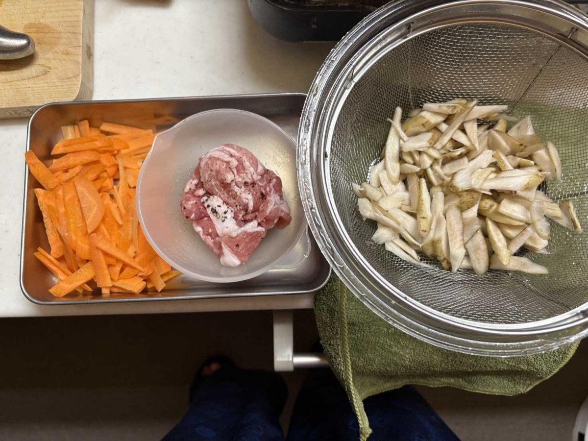 Prepped ingredients — julienned carrot, sliced pork belly, and shaved burdock draining in a strainer
