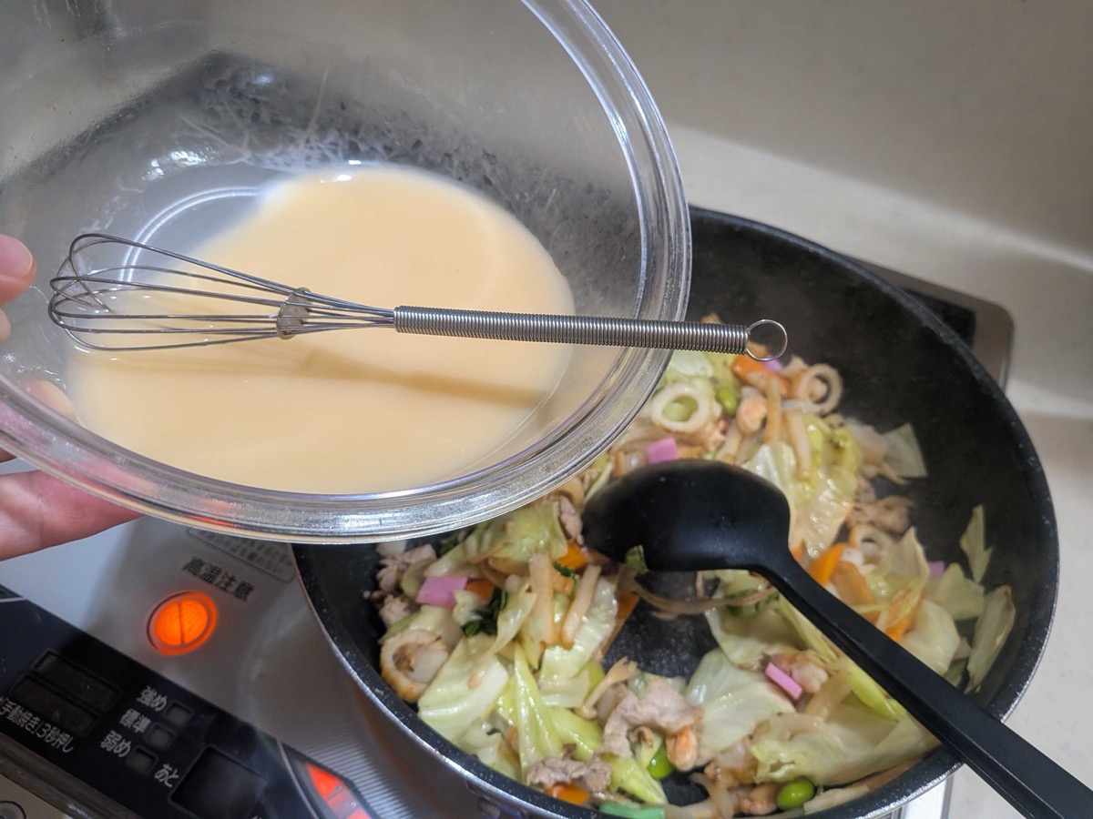 The ankake soup mixture being poured into the pan of stir-fried vegetables and seafood