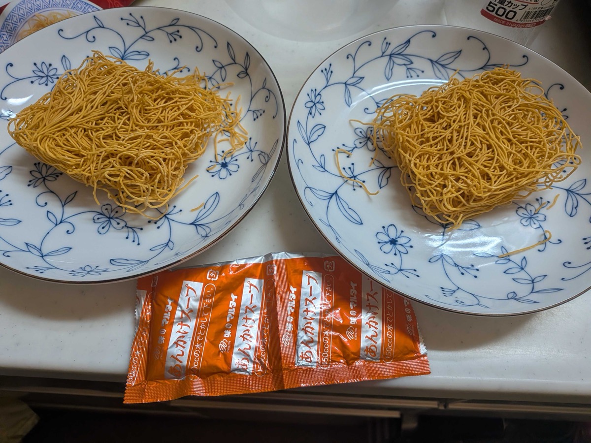 Crispy fried sara udon noodles portioned onto two plates with the ankake soup packets
