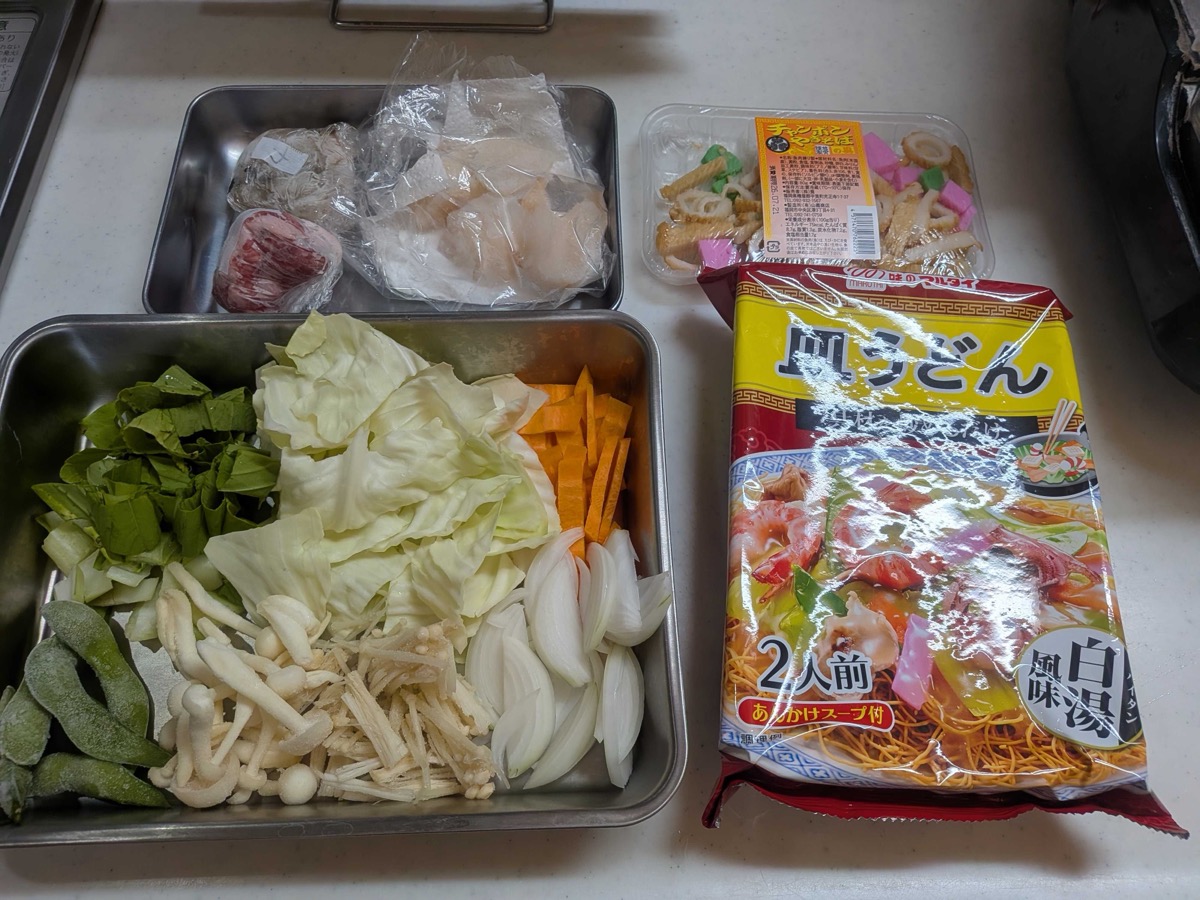 Sara udon ingredients laid out — pork, seafood, a tray of vegetables, and a Marutai sara udon kit