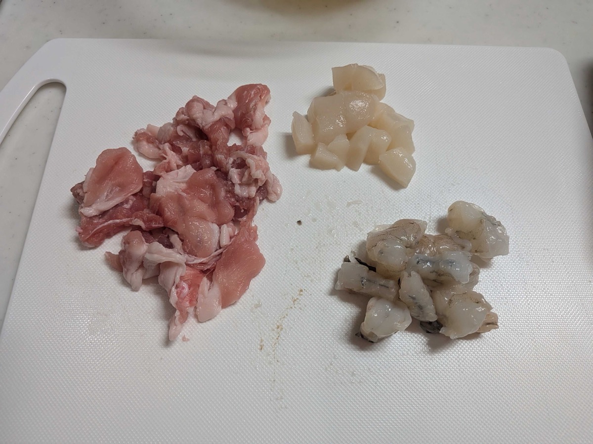 Thinly sliced pork, scallops, and shrimp on a cutting board