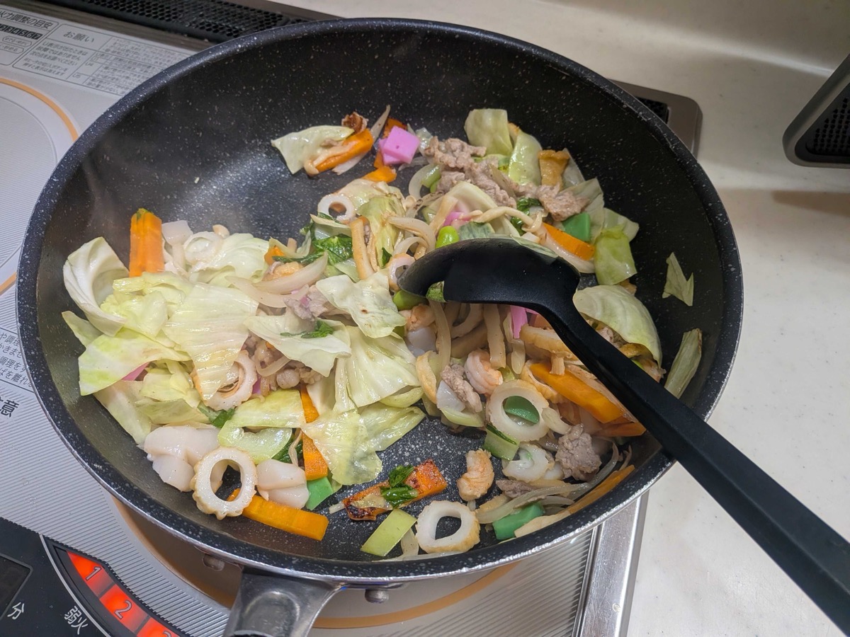 Cabbage, seafood, and fish cake added to the stir-fry in the pan