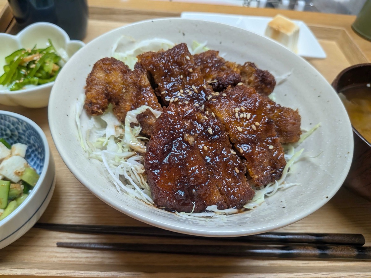 A bowl of Japanese sauce katsudon — sauce-glazed pork cutlet sliced over shredded cabbage and rice, sprinkled with sesame, with miso soup and side dishes