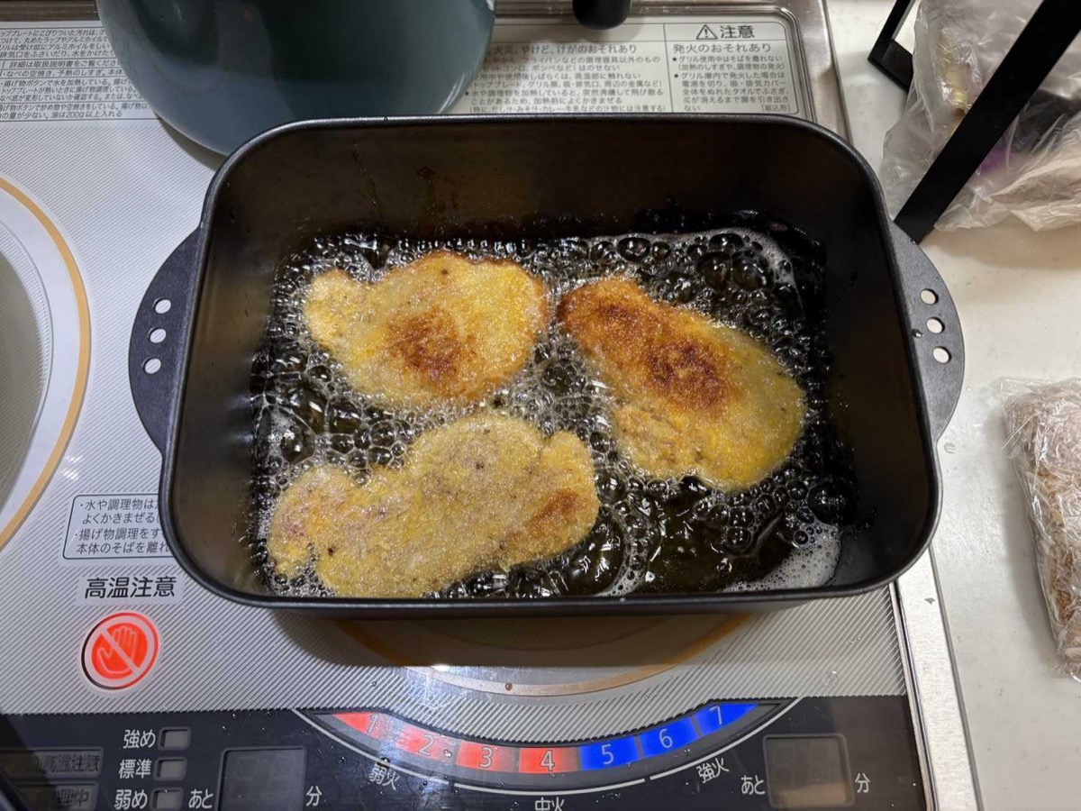 Panko-breaded pork cutlets frying to golden brown in oil