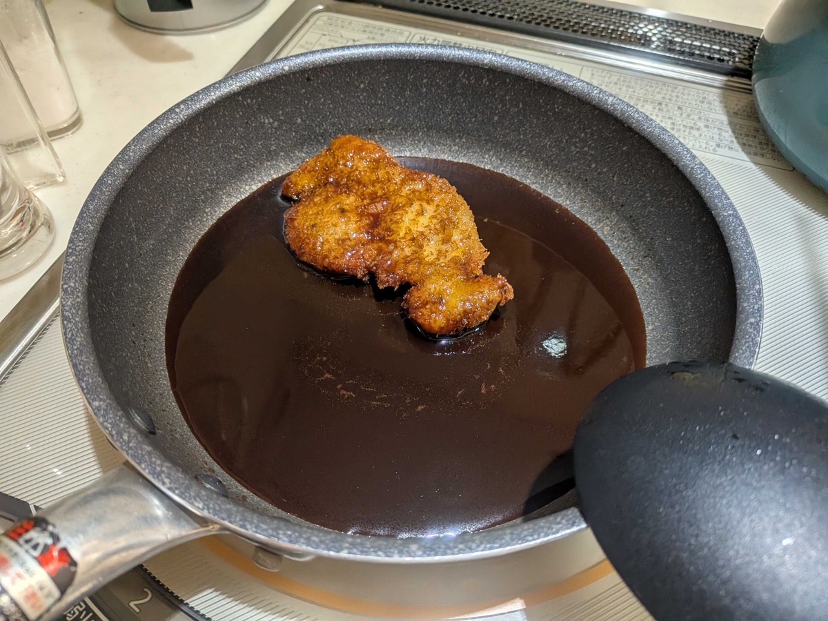 A pork cutlet fully coated in glossy dark katsudon sauce in the pan