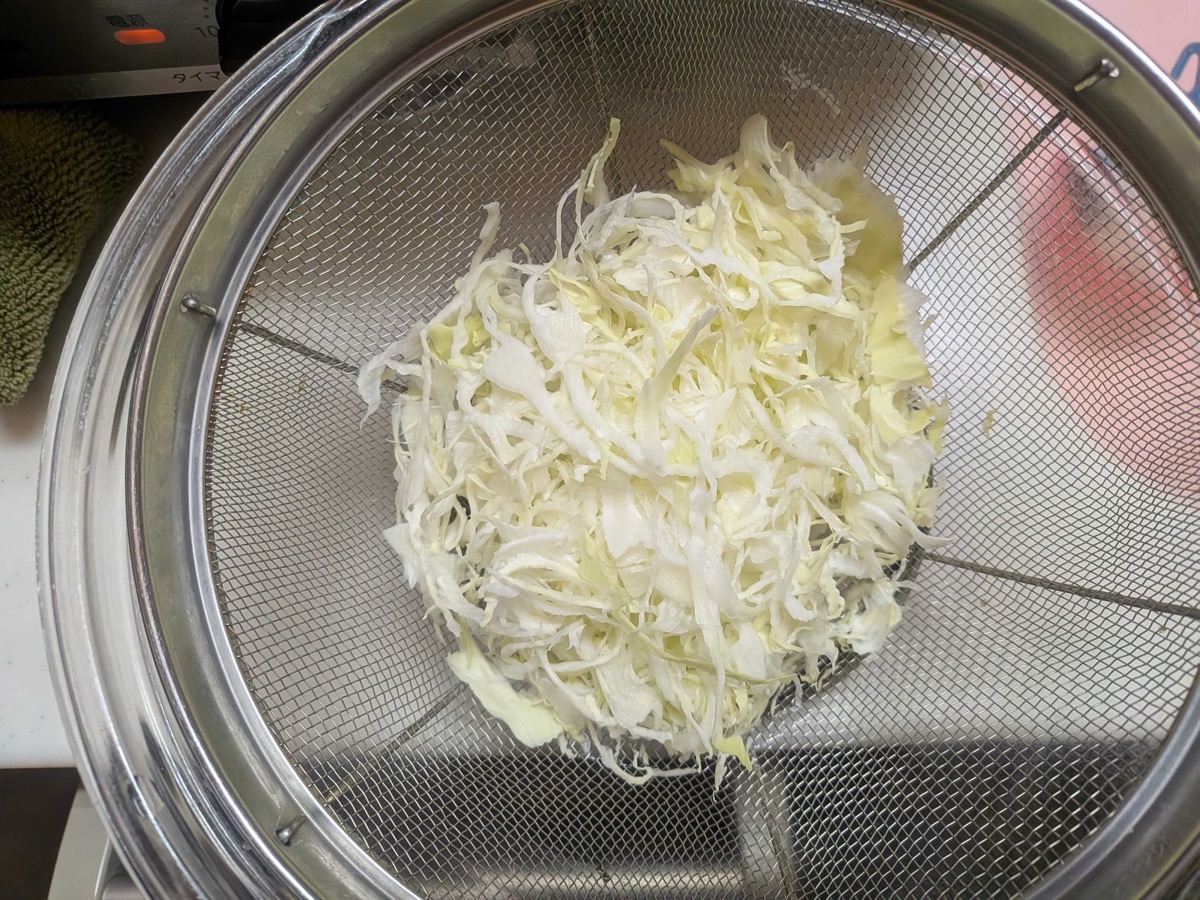 Finely shredded cabbage draining in a metal sieve