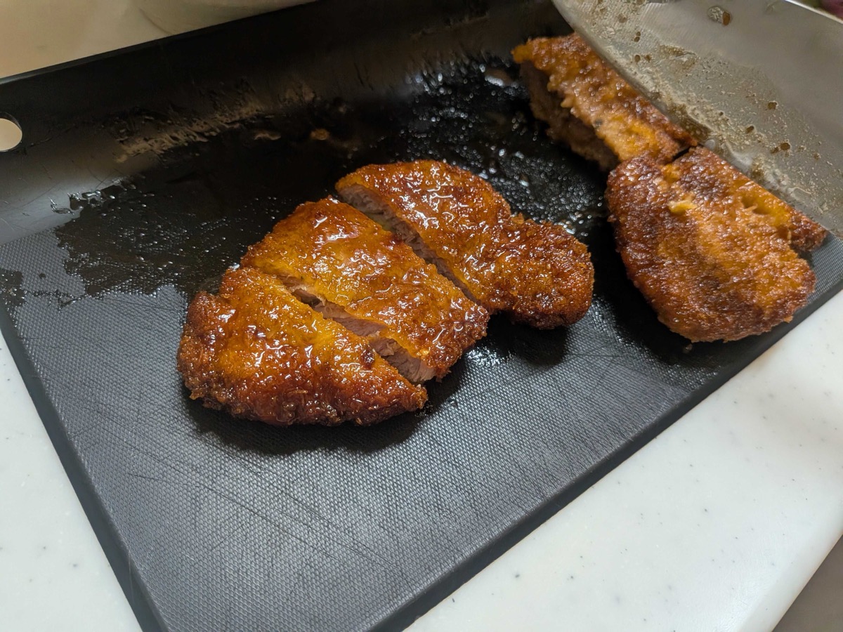 Sauce-coated pork cutlet sliced into strips on a black cutting board