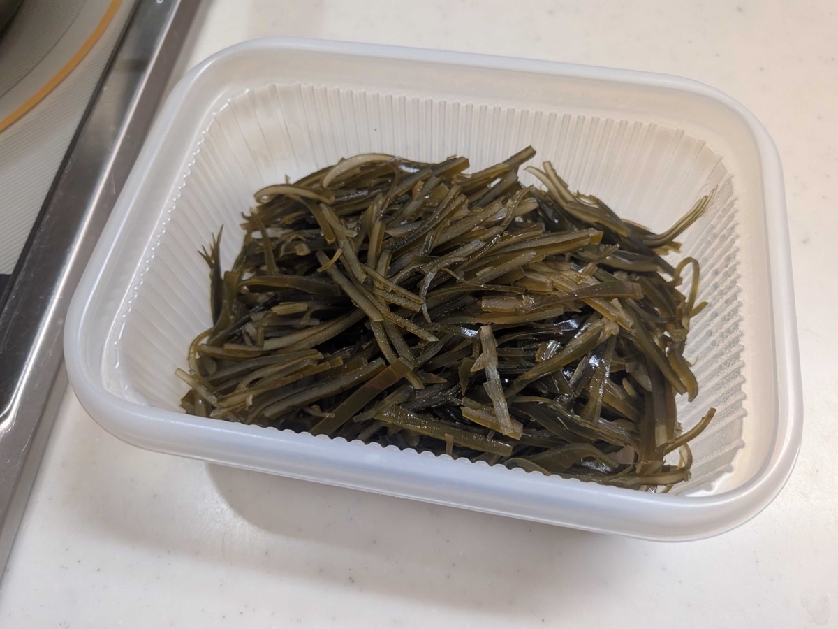 Leftover kombu from making Japanese dashi, sliced into thin dark green strips and piled in a white plastic container — the starting point for homemade shio kombu