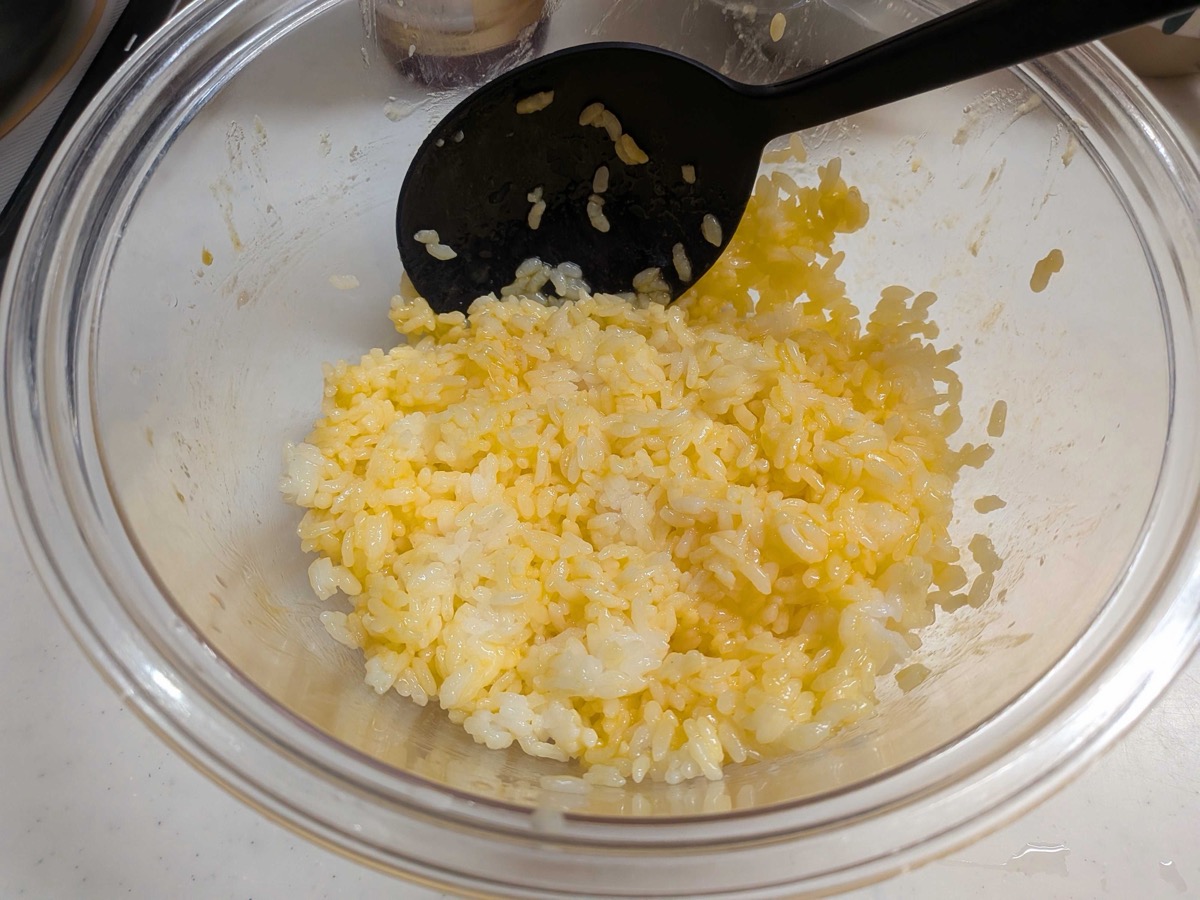 Cooked rice thoroughly mixed with beaten egg, turned pale yellow, in a glass bowl