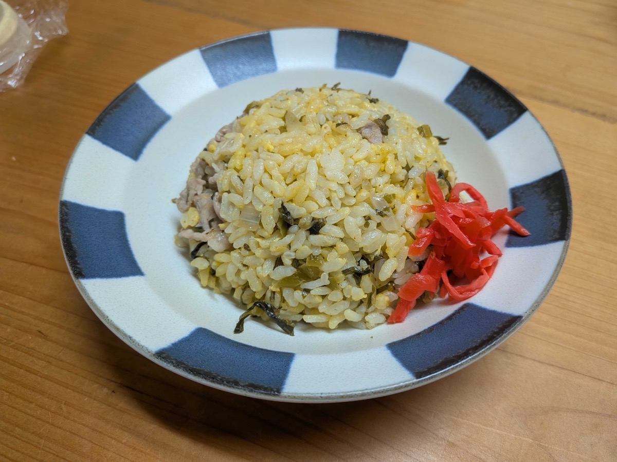 A plate of finished Japanese takana chahan — golden fried rice with pickled mustard greens and pork — mounded on a blue-and-white striped plate with a small pile of red pickled ginger