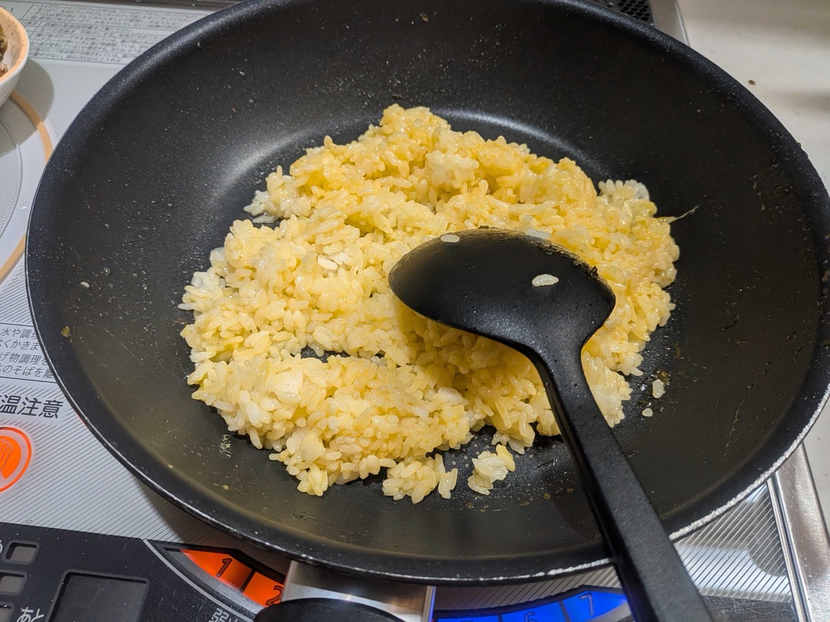 Golden egg-coated rice being stir-fried in a black frying pan until the grains separate