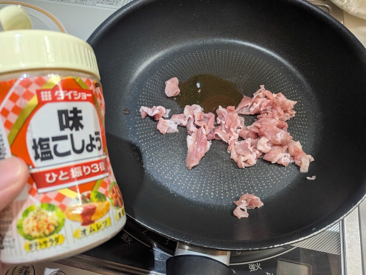Small pieces of pork frying in a pan, being seasoned with salt and pepper from a shaker