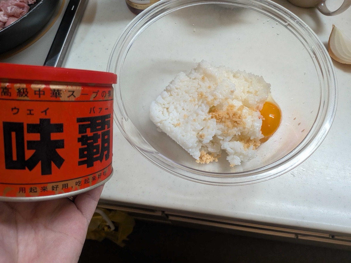 A bowl of cooked rice with a raw egg yolk and weipa Chinese soup base being added, with the red weipa can held alongside