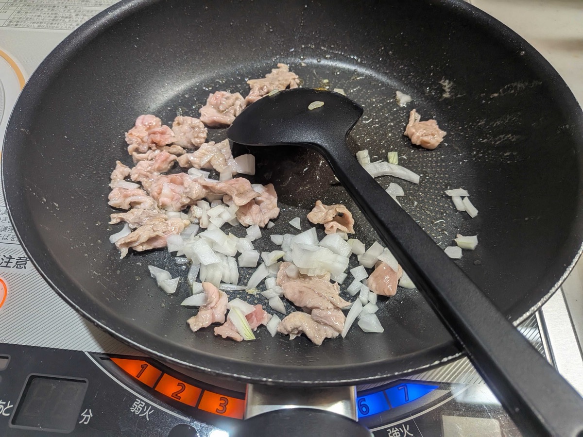 Pork and chopped onion being stir-fried together in a frying pan