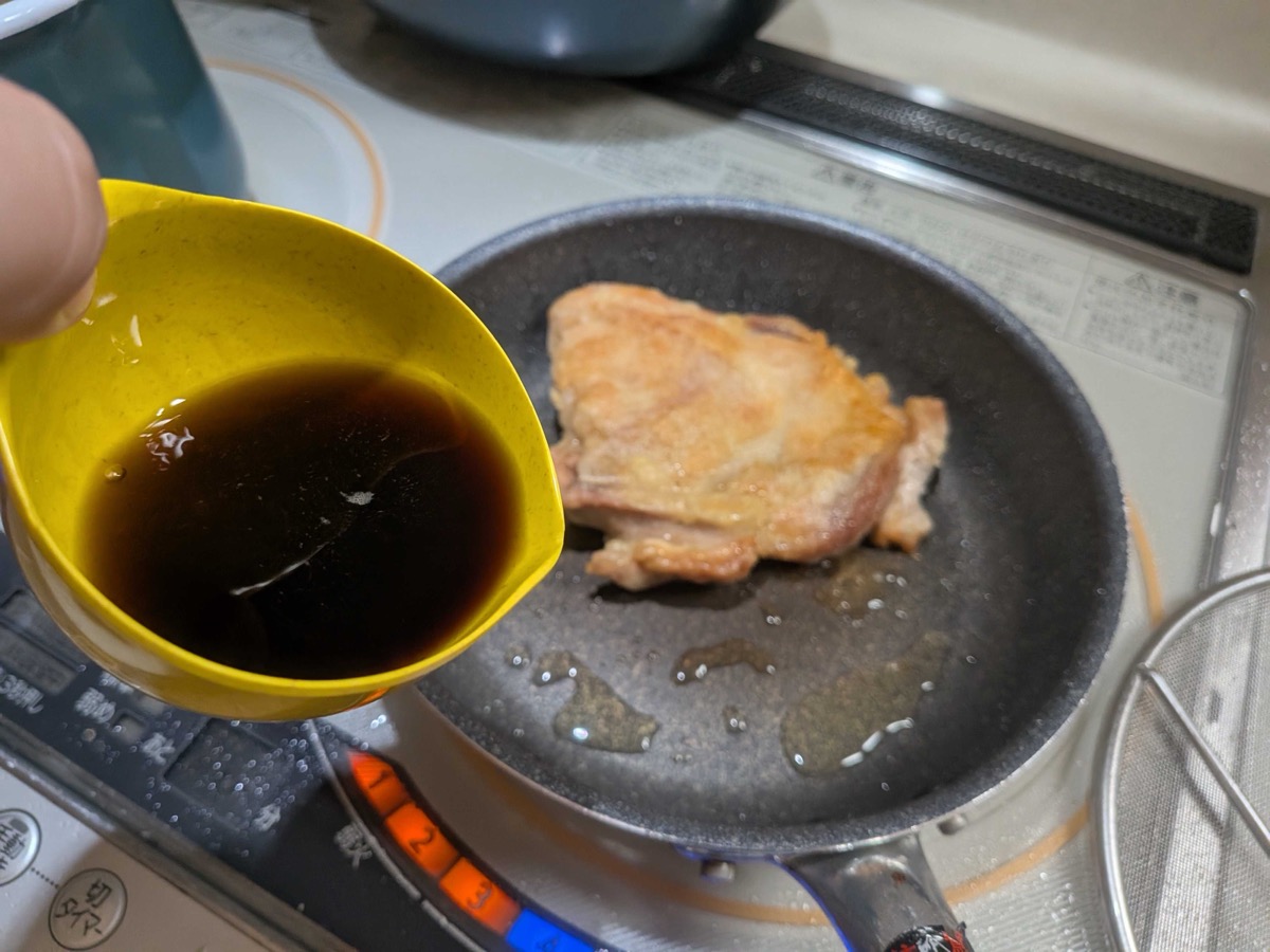 Teriyaki sauce being poured from a small yellow bowl into the pan with the browned chicken