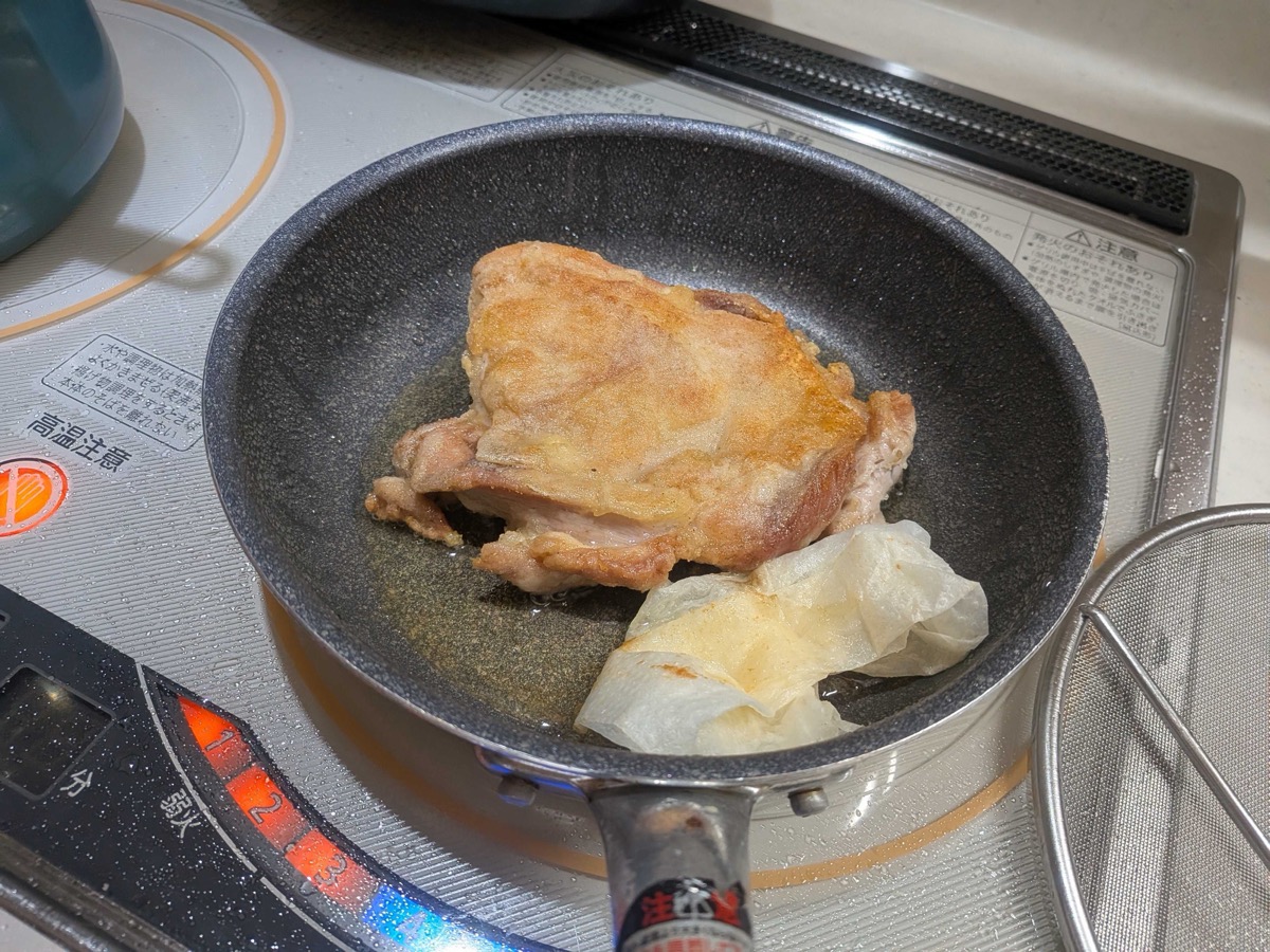 Golden browned chicken skin in the pan, with a paper towel wiping up excess oil
