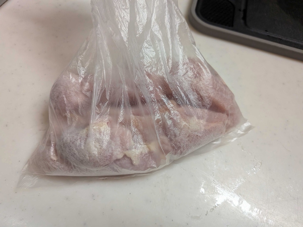 Chicken thigh being coated with potato starch in a plastic bag