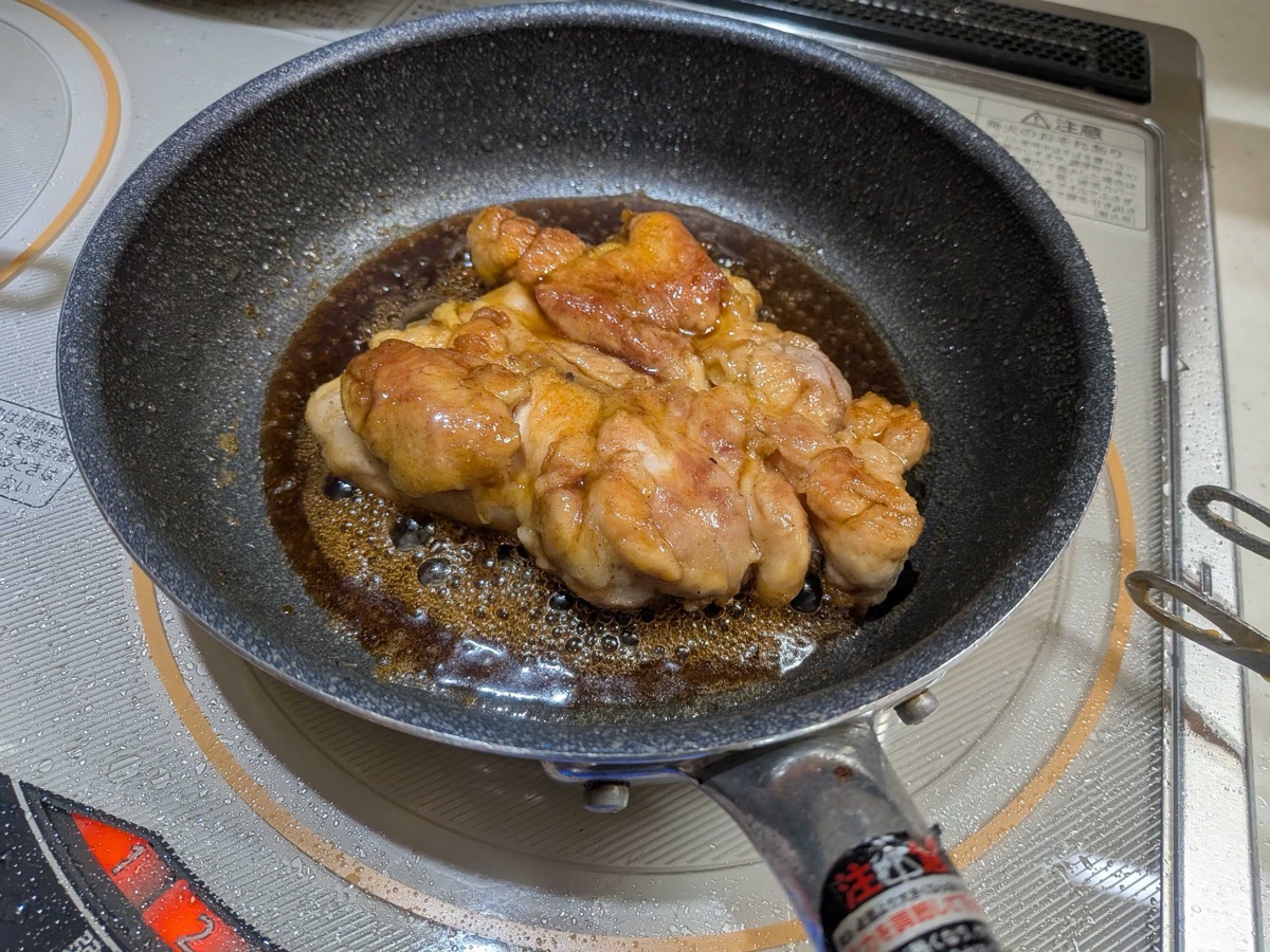Chicken thigh being glazed in the thickening teriyaki sauce