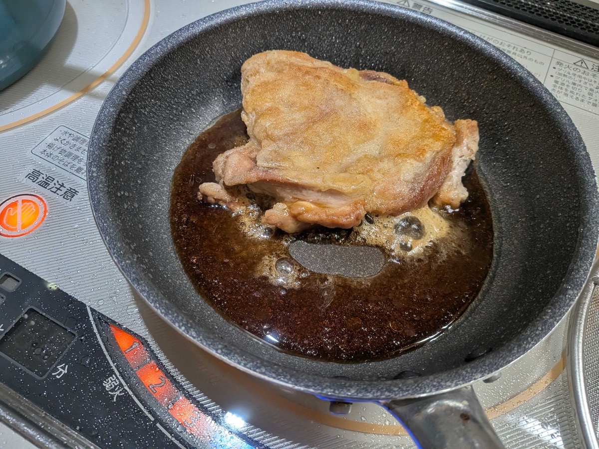 Chicken thigh simmering in the reducing teriyaki sauce in the pan