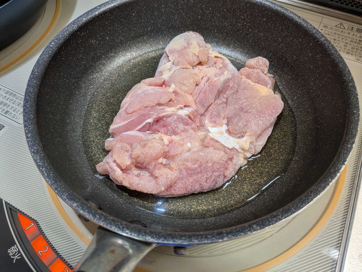 Chicken thigh laid skin-side down in a frying pan with oil