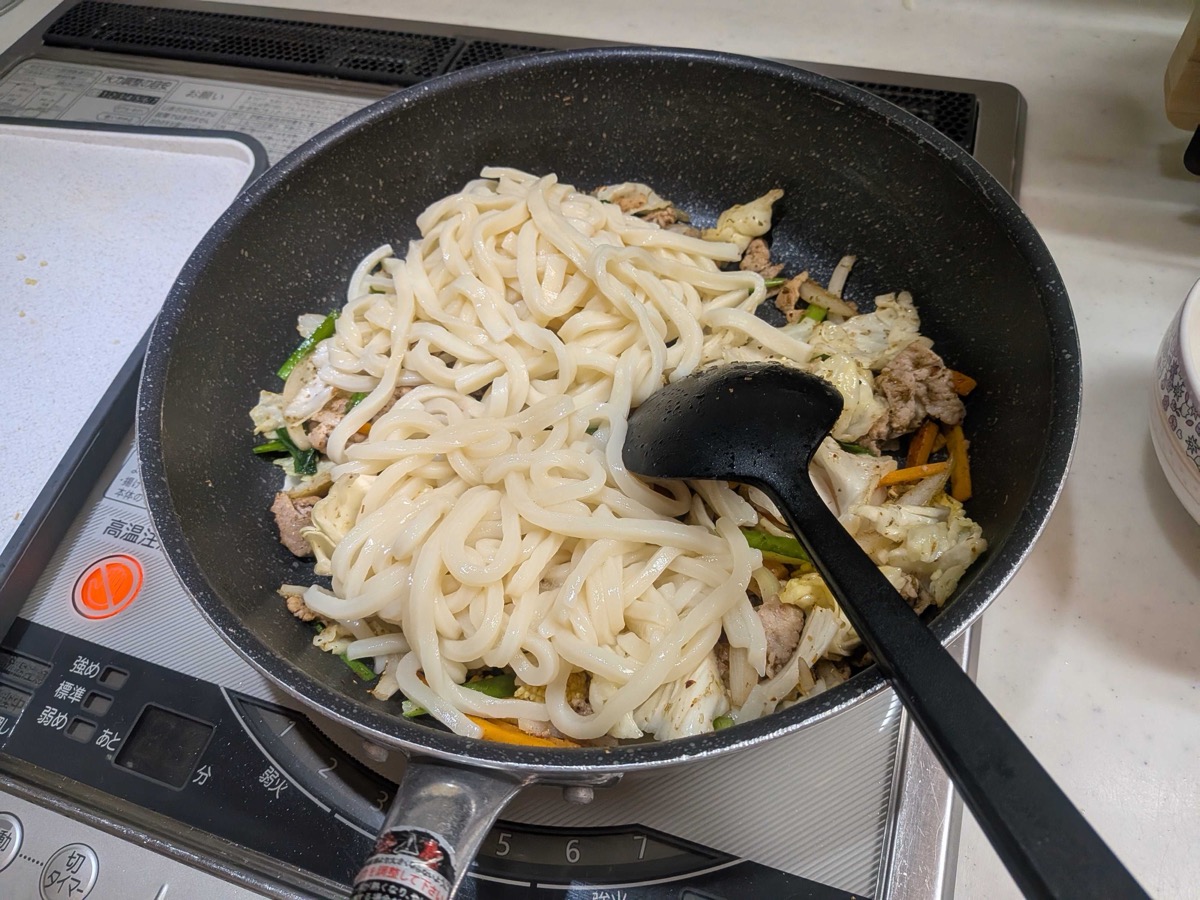 Warmed udon noodles added on top of the stir-fried pork and vegetables in the pan