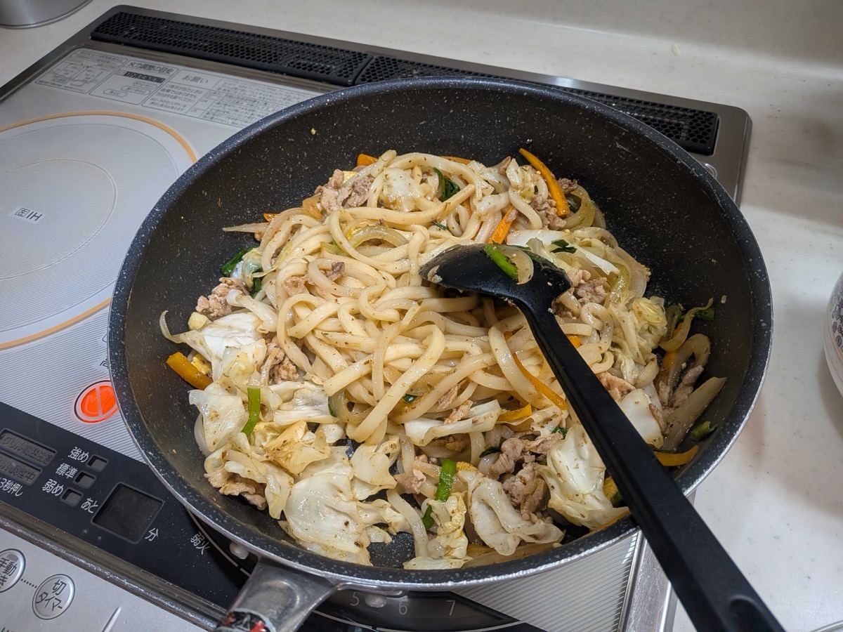 Finished yakiudon tossed together in the pan — udon noodles coated in seasoning with pork, cabbage, carrot, and garlic chives