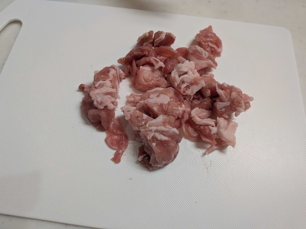 Thinly sliced pork cut into bite-sized pieces on a white cutting board