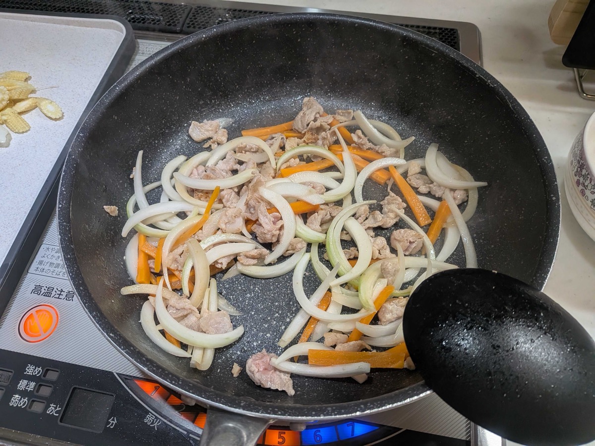 Pork, sliced onion, and carrot batons being stir-fried together in a frying pan
