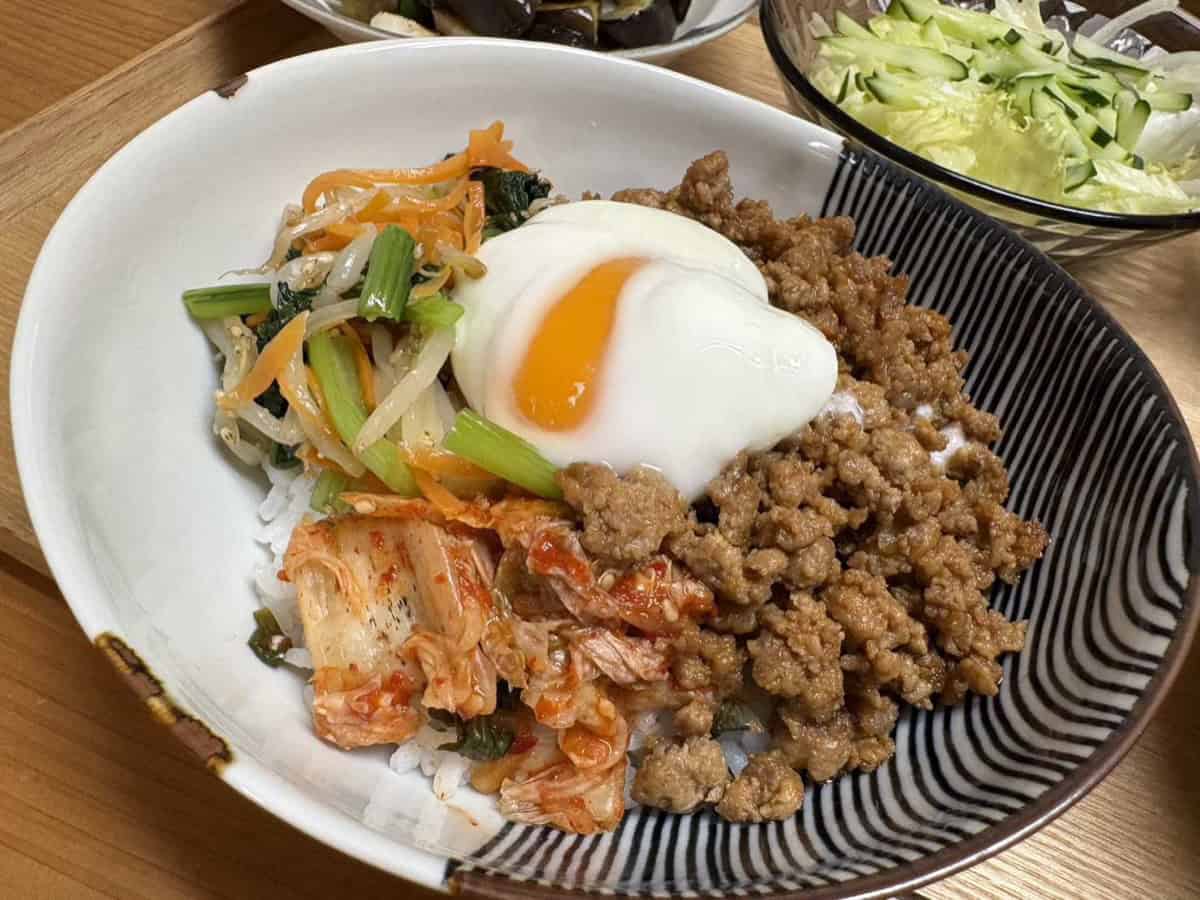 Assembled bibimbap bowl with meat, namul, kimchi, and a soft egg before mixing