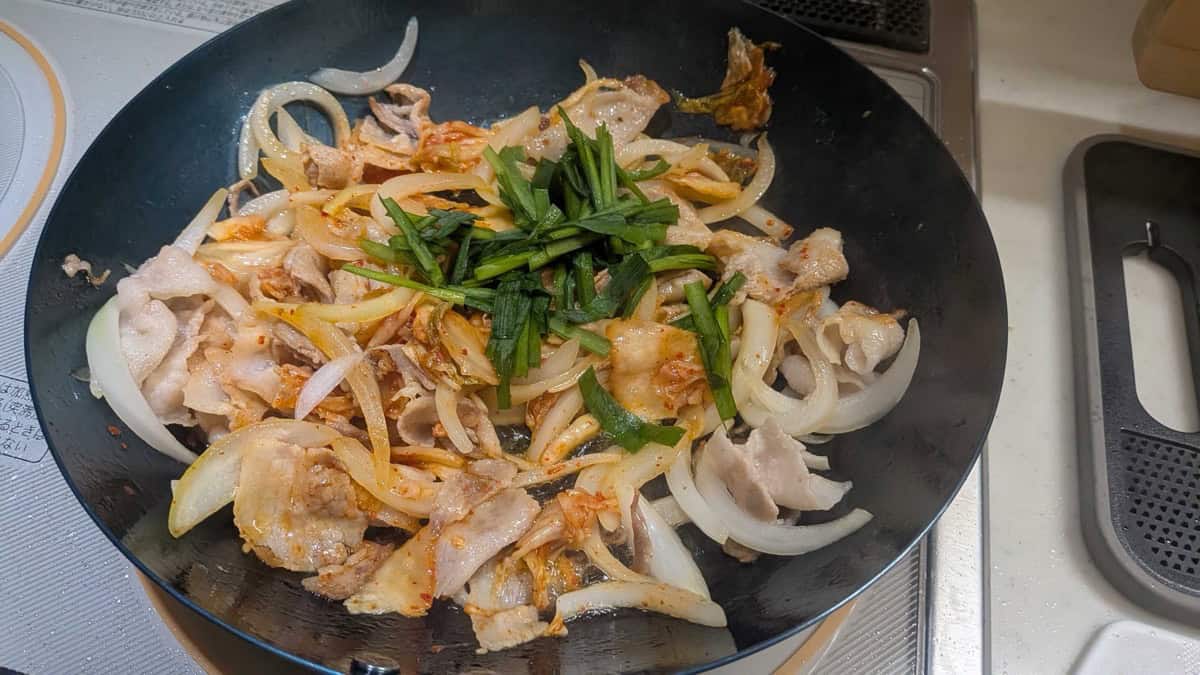 Cut garlic chives added on top of pork, onion and kimchi in the frying pan