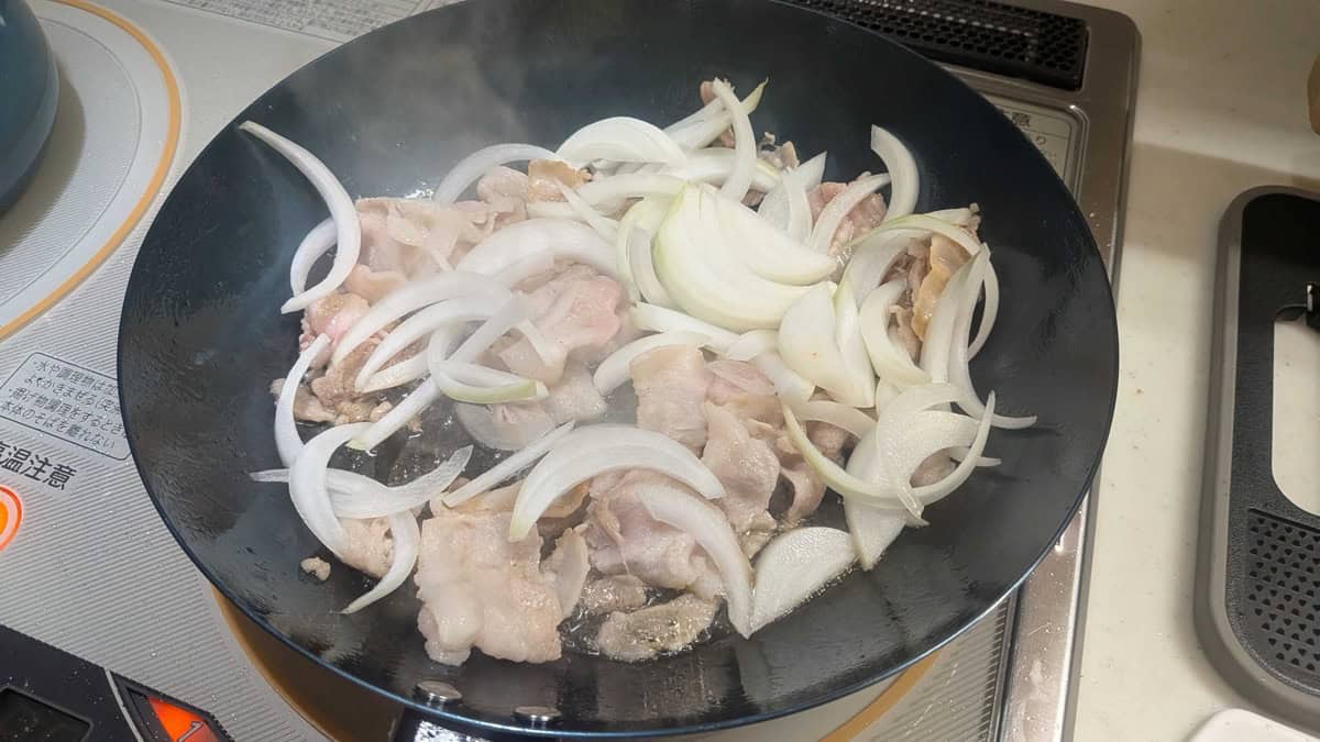 Sliced pork belly and onion just added to a hot frying pan on an IH cooktop