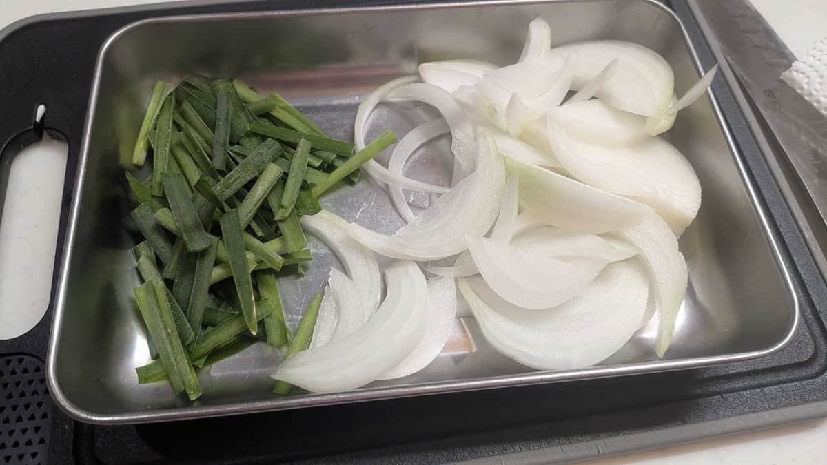 Cut garlic chives and thinly sliced onion arranged on a stainless steel tray