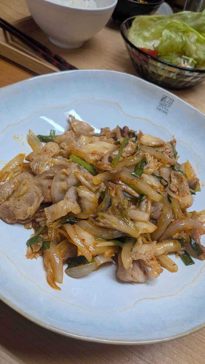 Buta kimchi — Japanese pork and kimchi stir-fry with onion and garlic chives, served on a blue plate with rice and salad