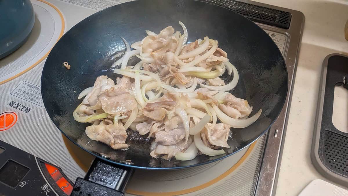 Pork belly cooked through and onion turned soft and translucent in a black frying pan