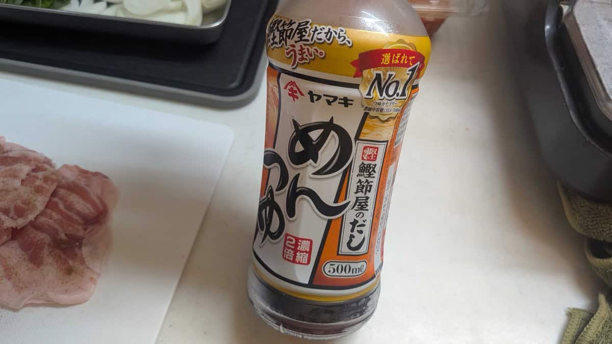 A bottle of Yamaki 2x concentrate mentsuyu noodle soup base on a kitchen counter next to sliced pork
