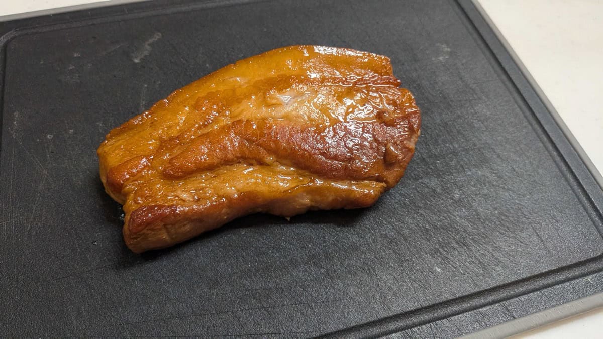 A glossy, deeply colored block of cooked chashu pork belly on a cutting board