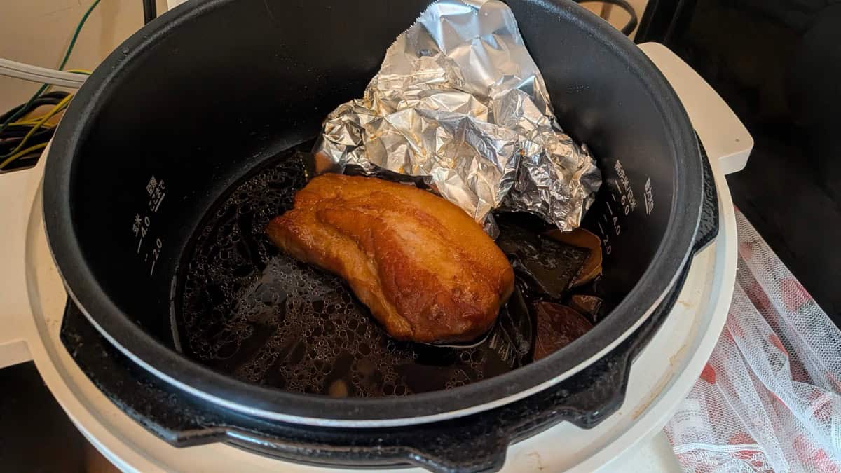 Cooked, deeply browned chashu resting in the pressure cooker pot with the foil drop-lid pushed aside