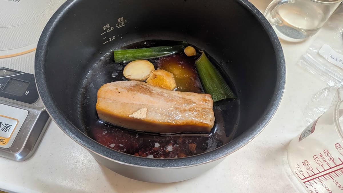 Seared pork belly in the pressure cooker inner pot with soy braising liquid, leek greens, and sliced ginger