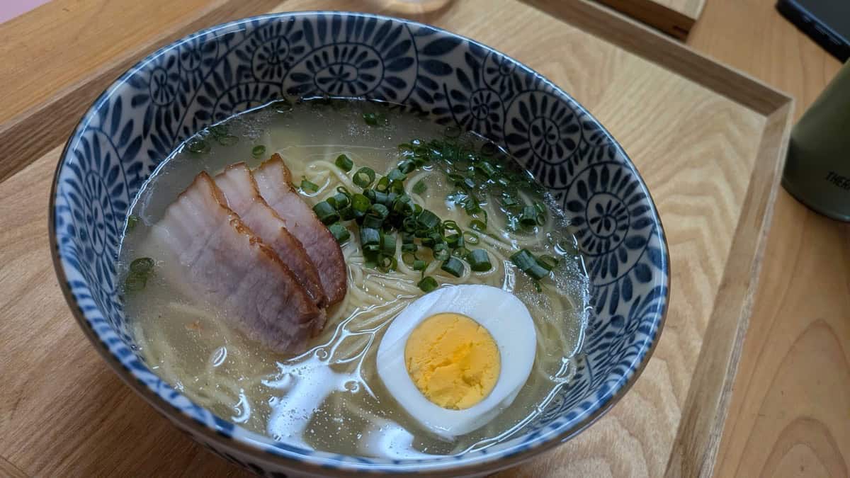 A bowl of shio ramen topped with slices of homemade chashu, a halved boiled egg, and chopped green onion