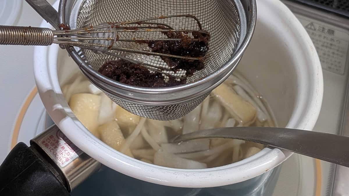Dissolving miso through a strainer into a pot of niban dashi to make miso soup