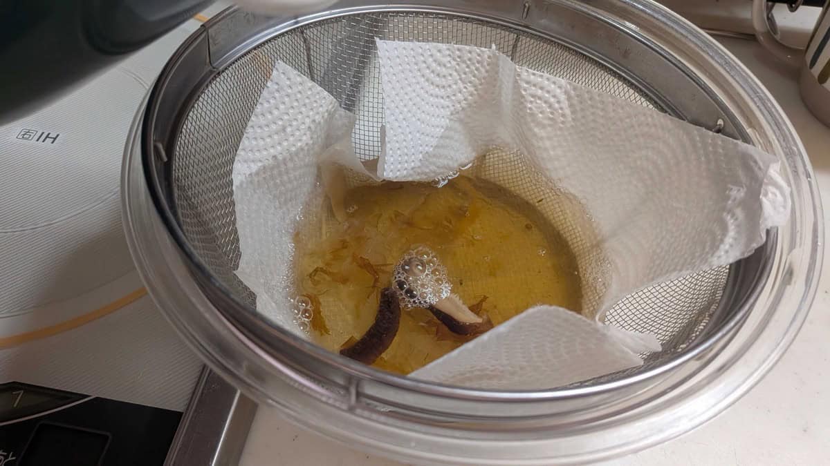 Straining the dashi through a paper-towel-lined sieve into a bowl