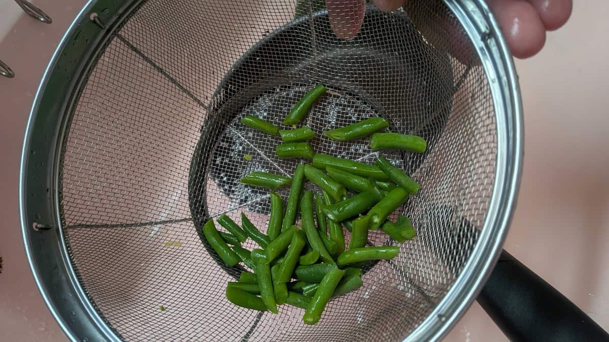 Boiled green beans draining in a mesh strainer in the sink