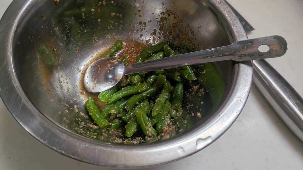 Green beans being tossed with the sesame dressing in a metal bowl