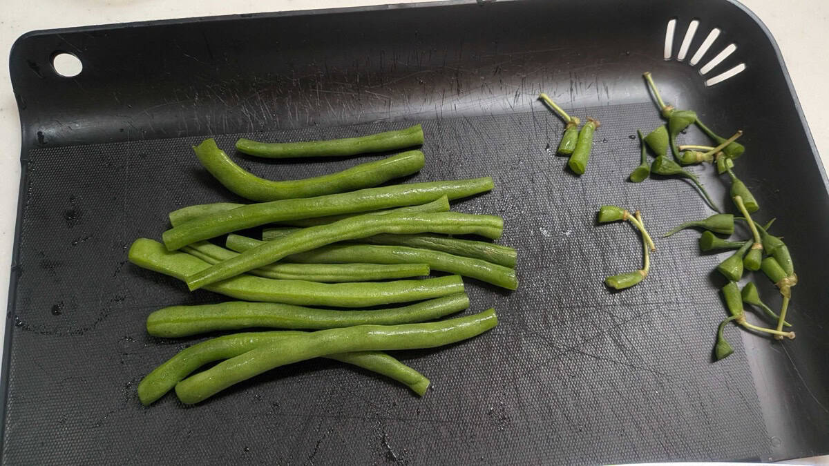 Green beans with the stem ends trimmed off and set aside on a cutting board