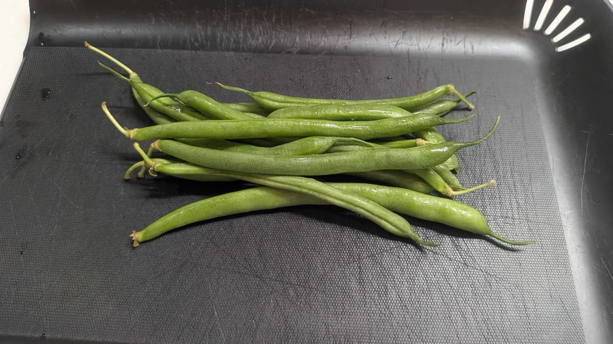 Fresh whole green beans on a black cutting board