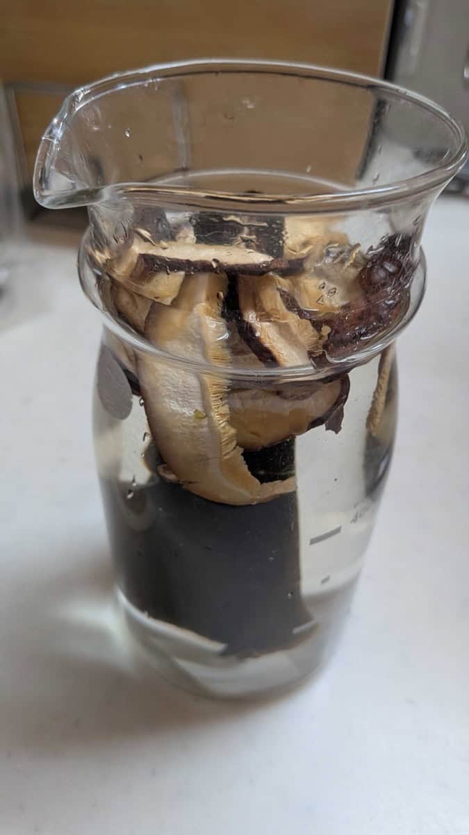 Kombu and dried shiitake mushrooms soaking in a glass jug of water to make a vegan dashi