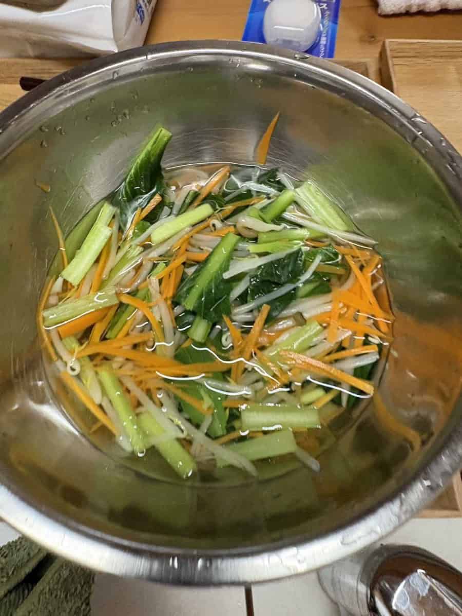 Blanched namul vegetables cooling in a bowl of water before being squeezed dry