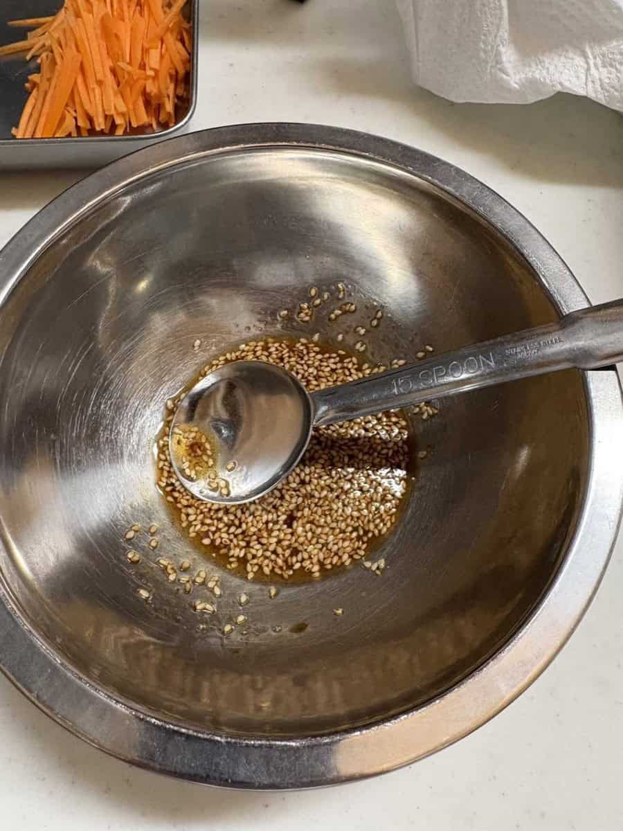 Mixing the namul seasoning — sesame oil, soy sauce, and sesame seeds in a metal bowl