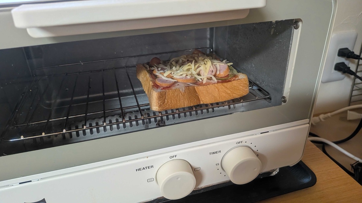 Pizza toast baking on the rack inside a small white countertop toaster oven