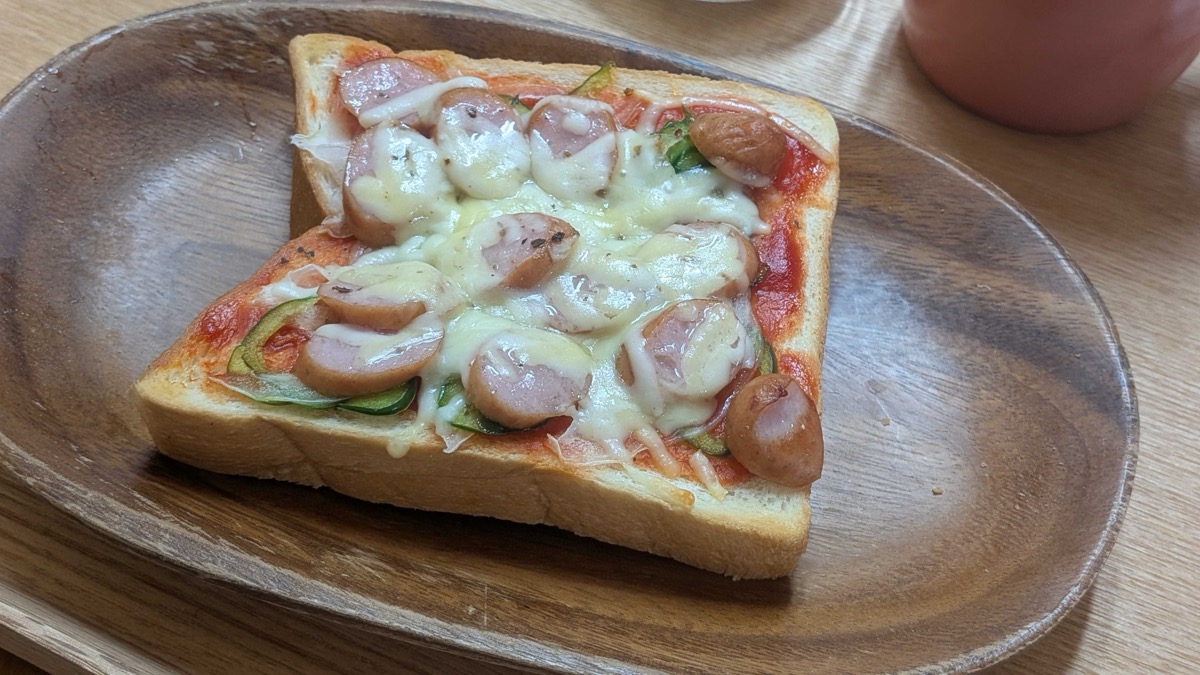 Finished pizza toast on a wooden plate with golden bubbling cheese and sausage rounds